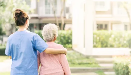 Caregiver supporting an elderly woman as they walk